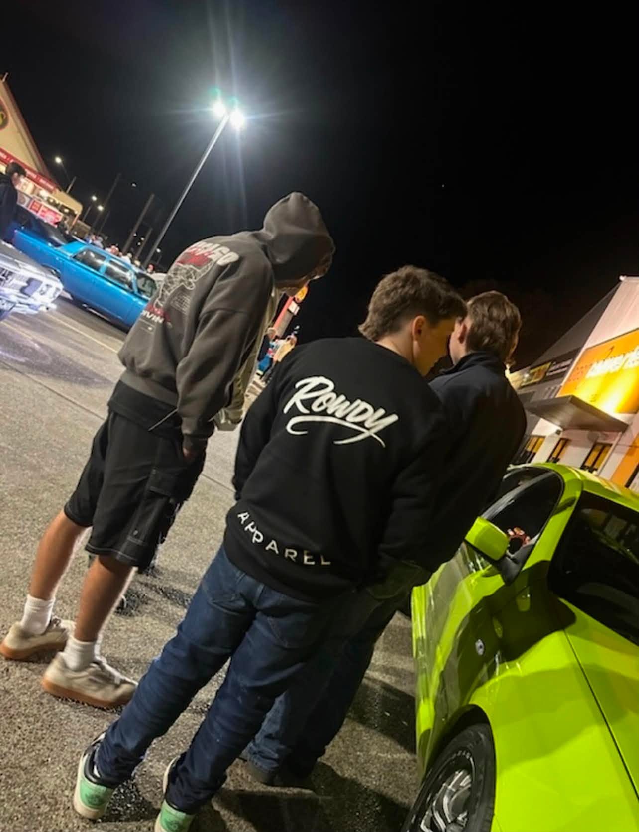 Rowdy Apparel hoodie at a night car meet beside a lime green car